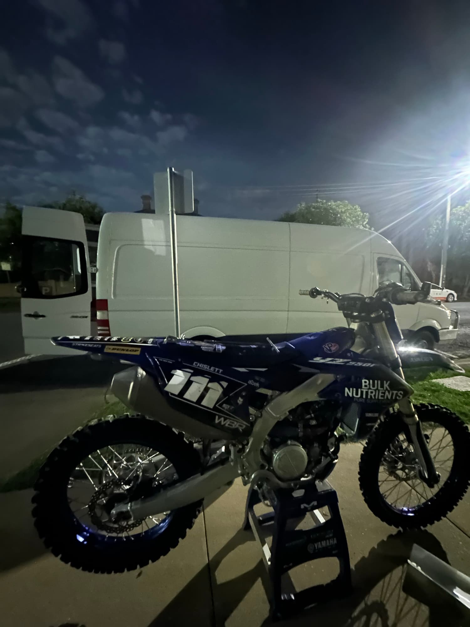 The number 111 Yamaha on a stand beside the van at night